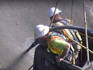 Two workers in a suspended platform spraying wet-mix shotcrete onto a vertical concrete surface