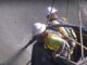 Two workers in a suspended platform spraying wet-mix shotcrete onto a vertical concrete surface