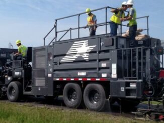 Crew operating a continuous slurry seal and microsurfacing paver applying a fresh preservation mat on a rural two-lane road
