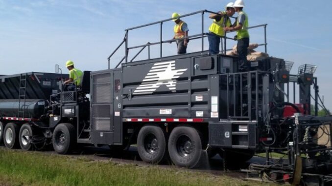 Crew operating a continuous slurry seal and microsurfacing paver applying a fresh preservation mat on a rural two-lane road