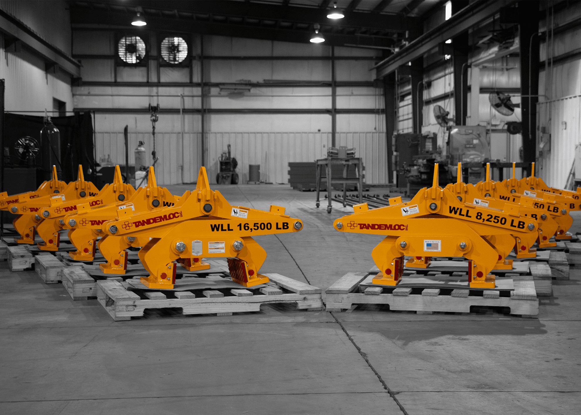 Yellow Tandemloc concrete barrier grabs on pallets marked WLL 16,500 LB and WLL 8,250 LB in a manufacturing facility