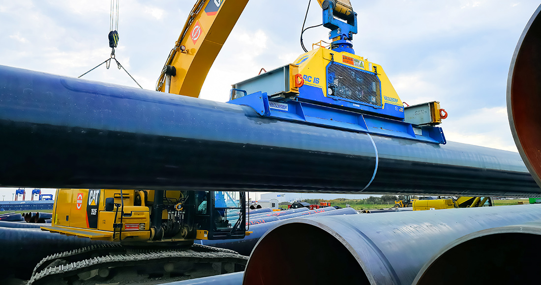 Excavator-mounted vacuum lifter sealed on a large-diameter coated steel pipe in a materials yard
