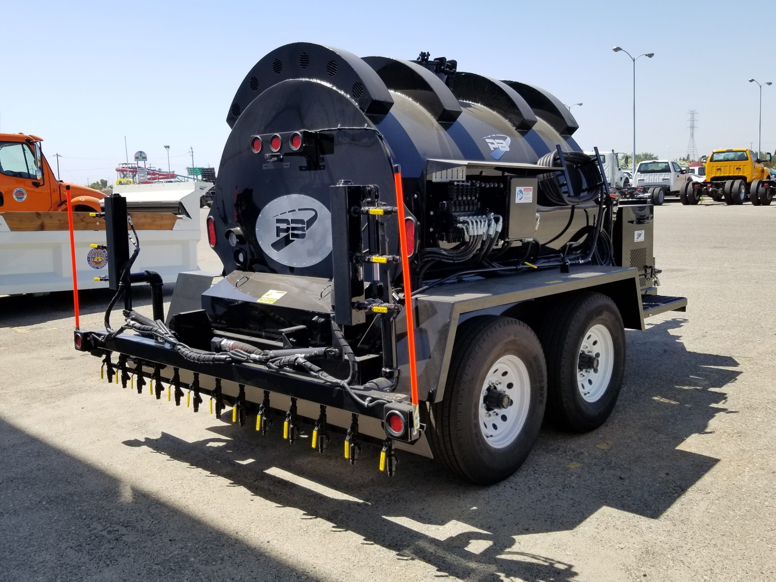 Black dual-axle PB Loader trailer emulsion sprayer with rear multi-nozzle spray bar