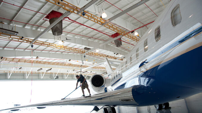 Technician in a harness on a jet wing connected to yellow overhead rigid-rail fall protection tracks in an aircraft hangar