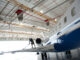 Technician in a harness on a jet wing connected to yellow overhead rigid-rail fall protection tracks in an aircraft hangar
