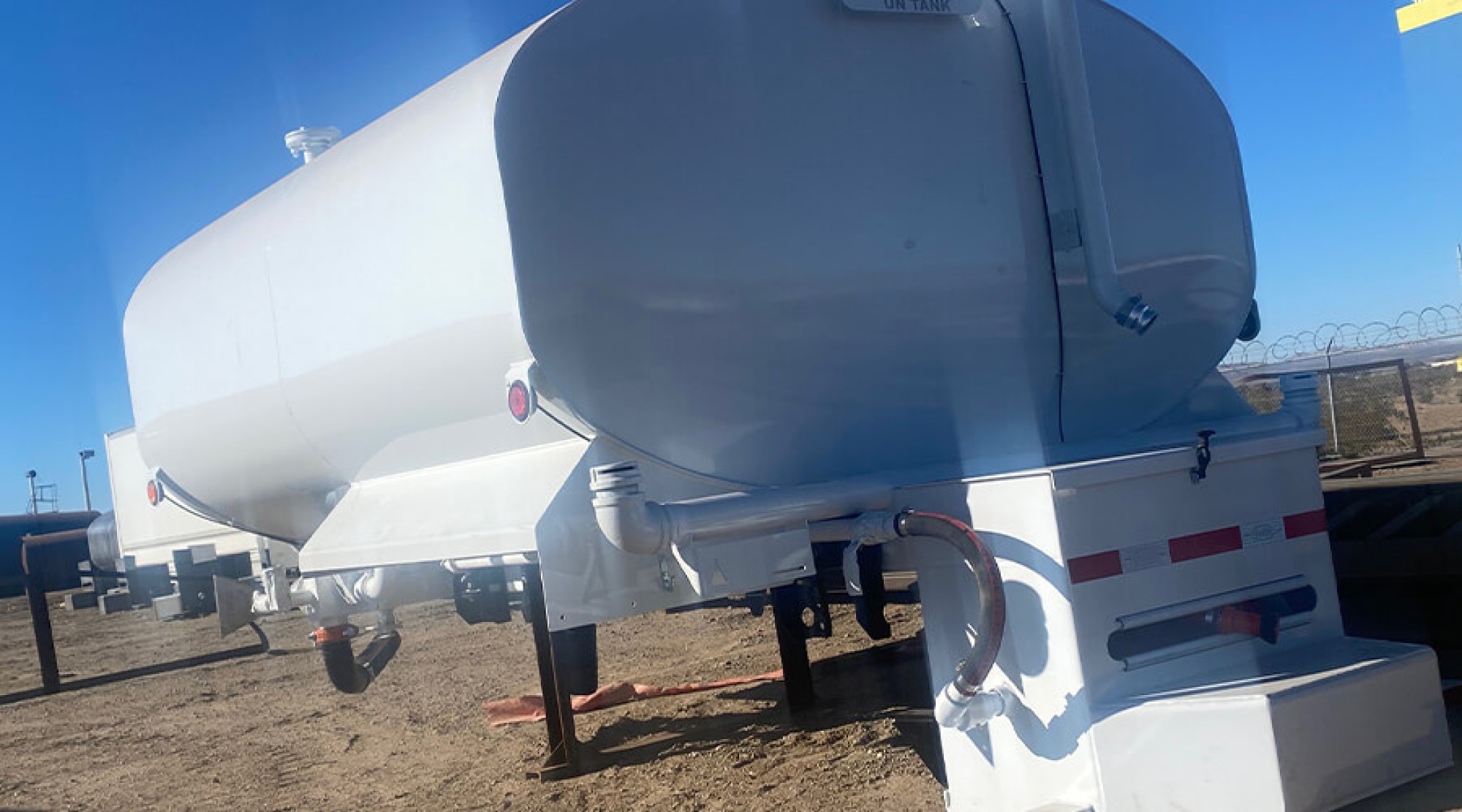 White Valew water tank body with plumbing and subframe sitting in an equipment yard