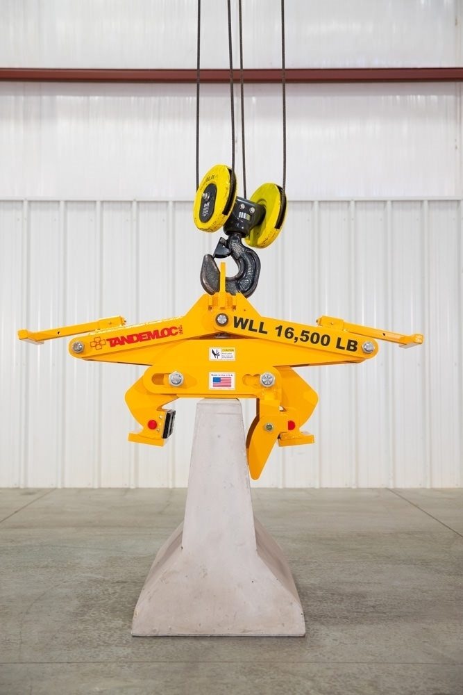 Yellow Tandemloc concrete barrier grab marked WLL 16,500 LB lifting a Jersey barrier from a crane hook