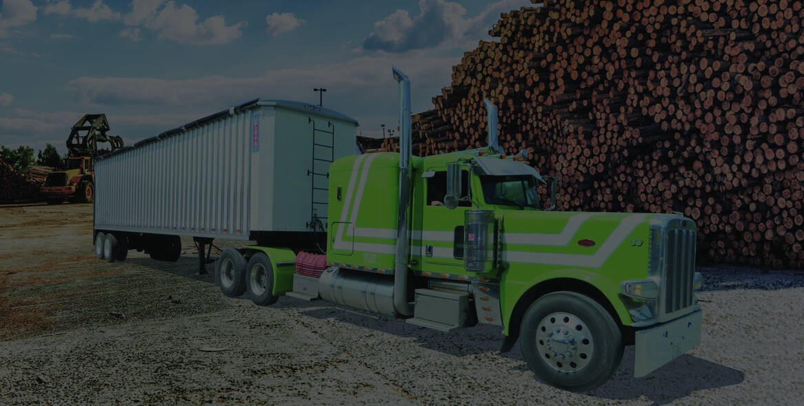 Lime-green Peterbilt tractor with white chip van trailer parked beside stacked logs at a timber yard