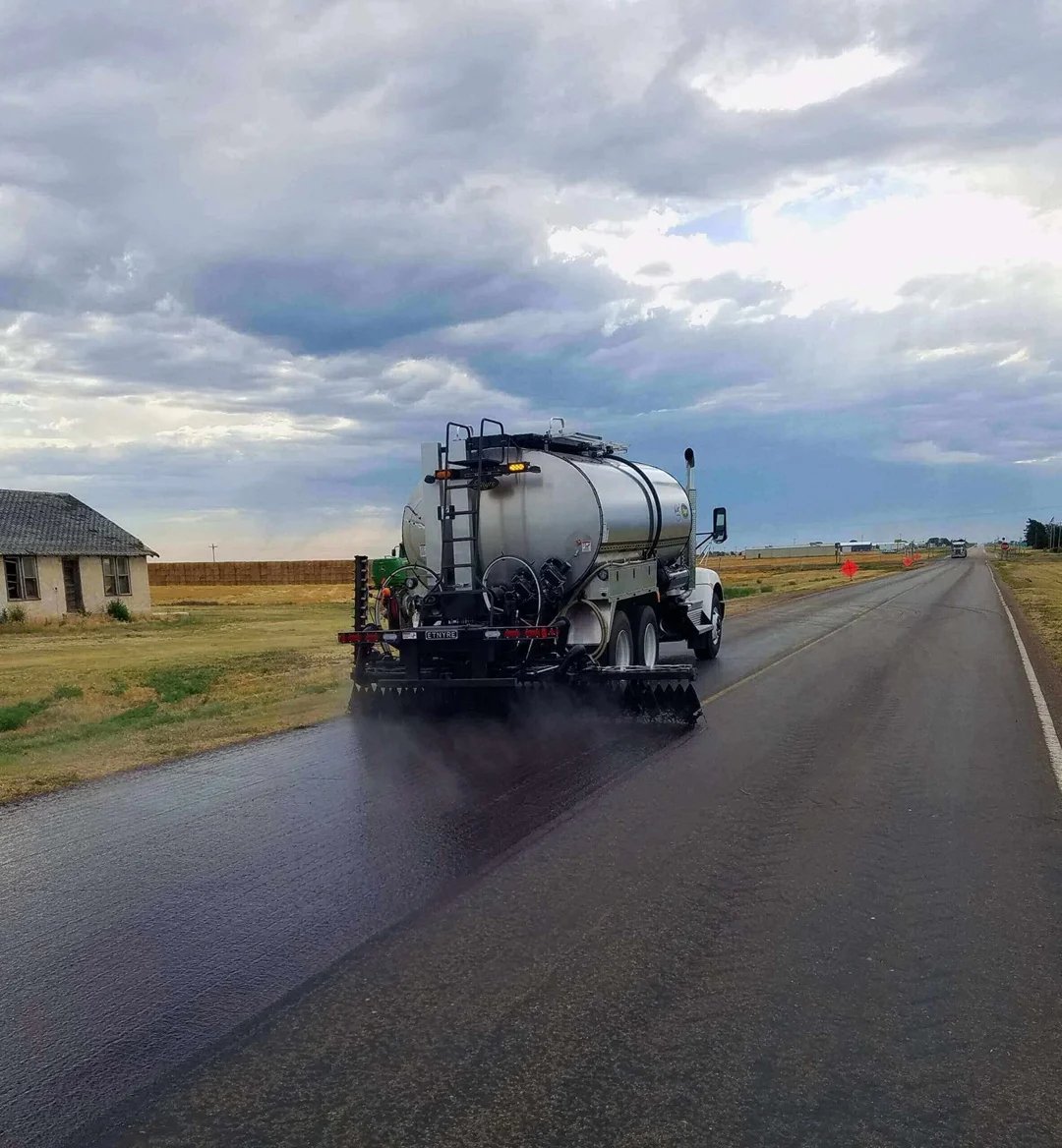 Etnyre asphalt distributor applying liquid asphalt across a lane on a rural road