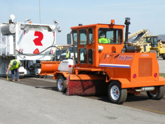 Construction broom sweeping milled asphalt behind a cold planer