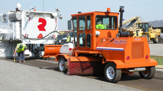 Construction broom sweeping milled asphalt behind a cold planer