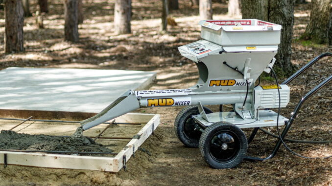 Gray MudMixer continuous concrete mixer discharging wet concrete into a wood-formed residential slab with rebar over sand outdoors