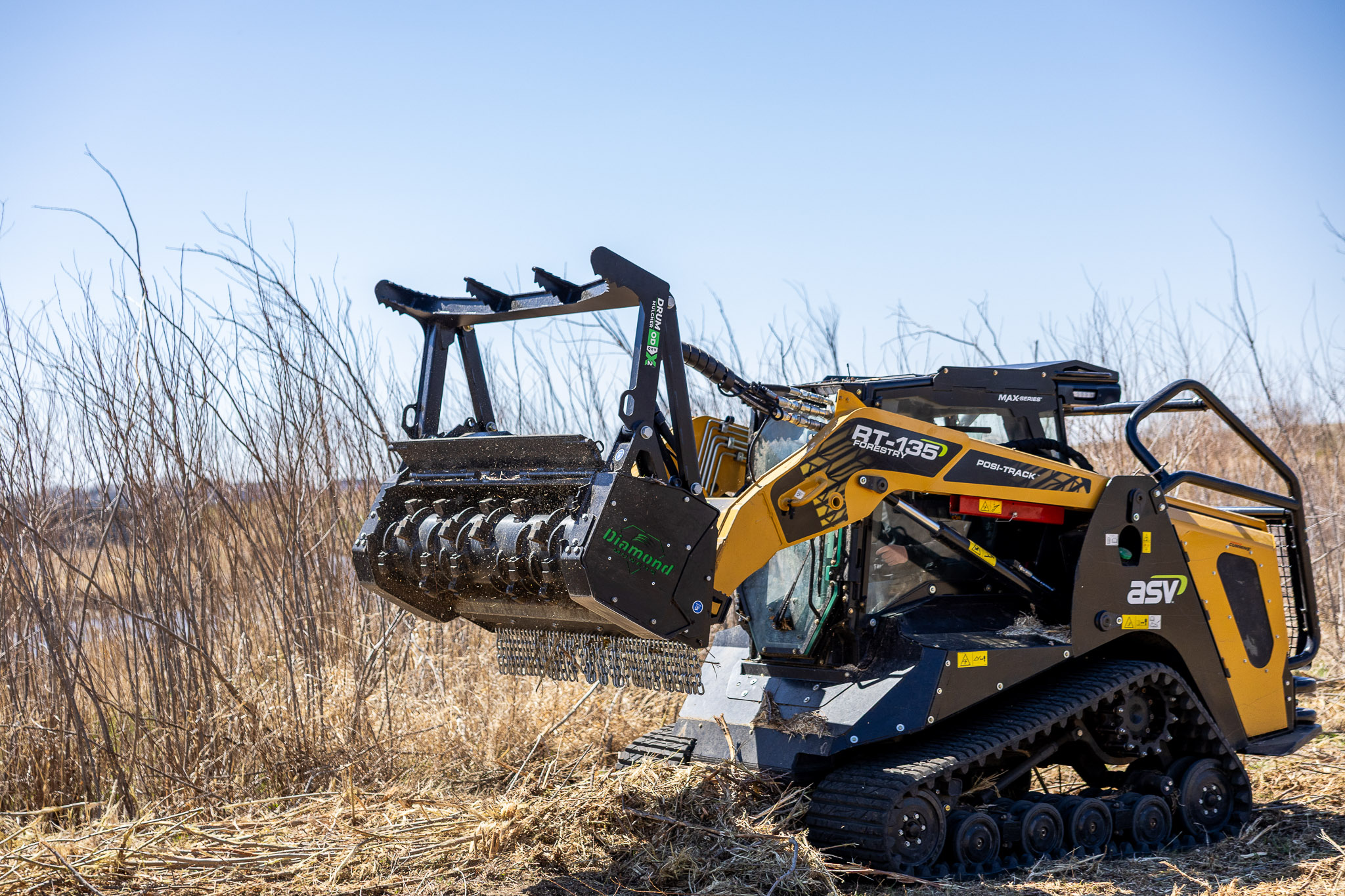 Open-drum skid-steer mulcher clearing brush with ground engagement