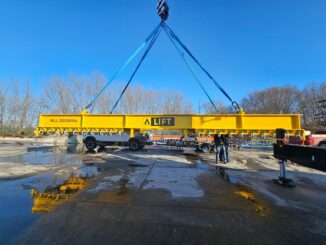Yellow A-Lift spreader beam suspended on blue slings over wet concrete yard with workers