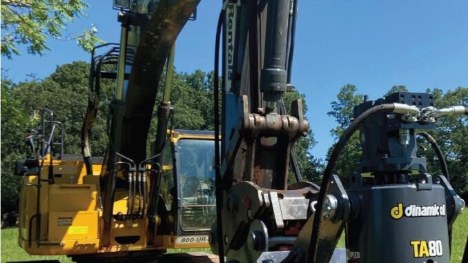 Dinamic Oil TA80 hydraulic auger drive mounted on yellow John Deere excavator in a grassy field