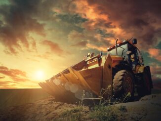 Yellow wheel loader on excavated earth with large OTR tire tread clearly visible at sunset