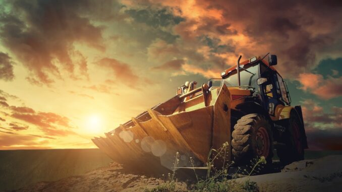 Yellow wheel loader on excavated earth with large OTR tire tread clearly visible at sunset