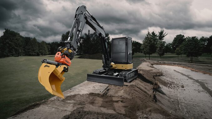 Compact excavator with orange tiltrotator and yellow AMI grading bucket working a sand-lined trench