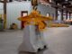 Yellow Tandemloc concrete barrier grab clamped on a gray Jersey barrier suspended from a crane hook in a warehouse