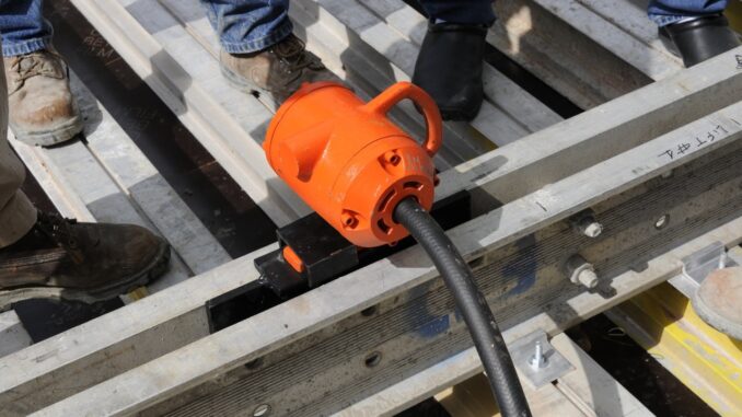 Orange external pneumatic form vibrator clamped between modular aluminum form rails on a precast pour