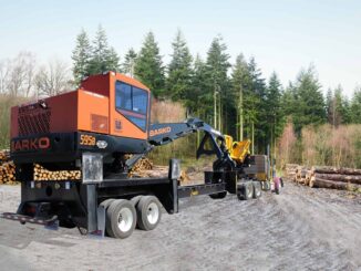 Orange Barko knuckle-boom log loader mounted on a multi-axle carrier trailer at a timber landing