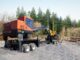 Orange Barko knuckle-boom log loader mounted on a multi-axle carrier trailer at a timber landing