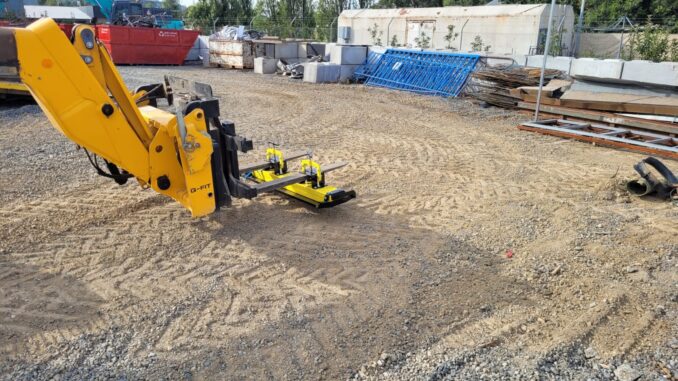 Yellow forklift-mounted magnetic sweeper hovering over gravel in an industrial yard with scrap bins and concrete blocks