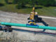 Excavator with vacuum lifter unloading large-diameter coated pipe from a flatbed trailer on a pipeline right-of-way