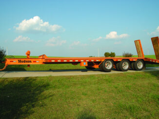 Orange Hudson equipment trailer with dual rear loading ramps on a rural driveway