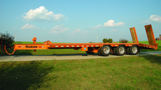 Orange Hudson equipment trailer with dual rear loading ramps on a rural driveway