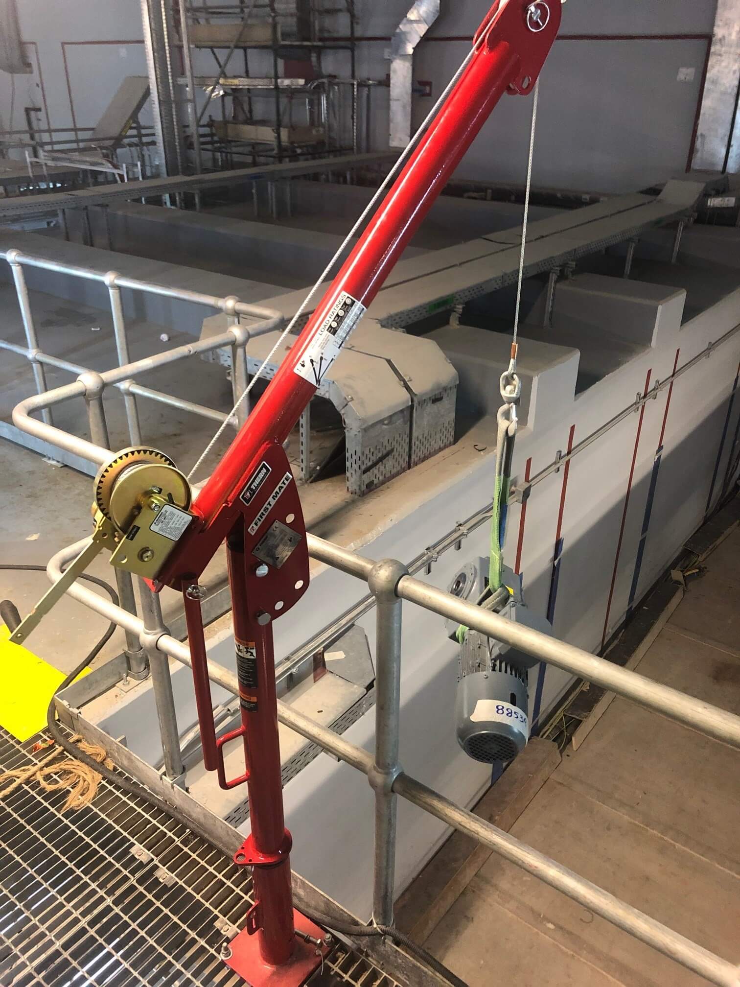 Red Thern First Mate davit crane on a grated walkway lifting a grey electric motor with a green sling