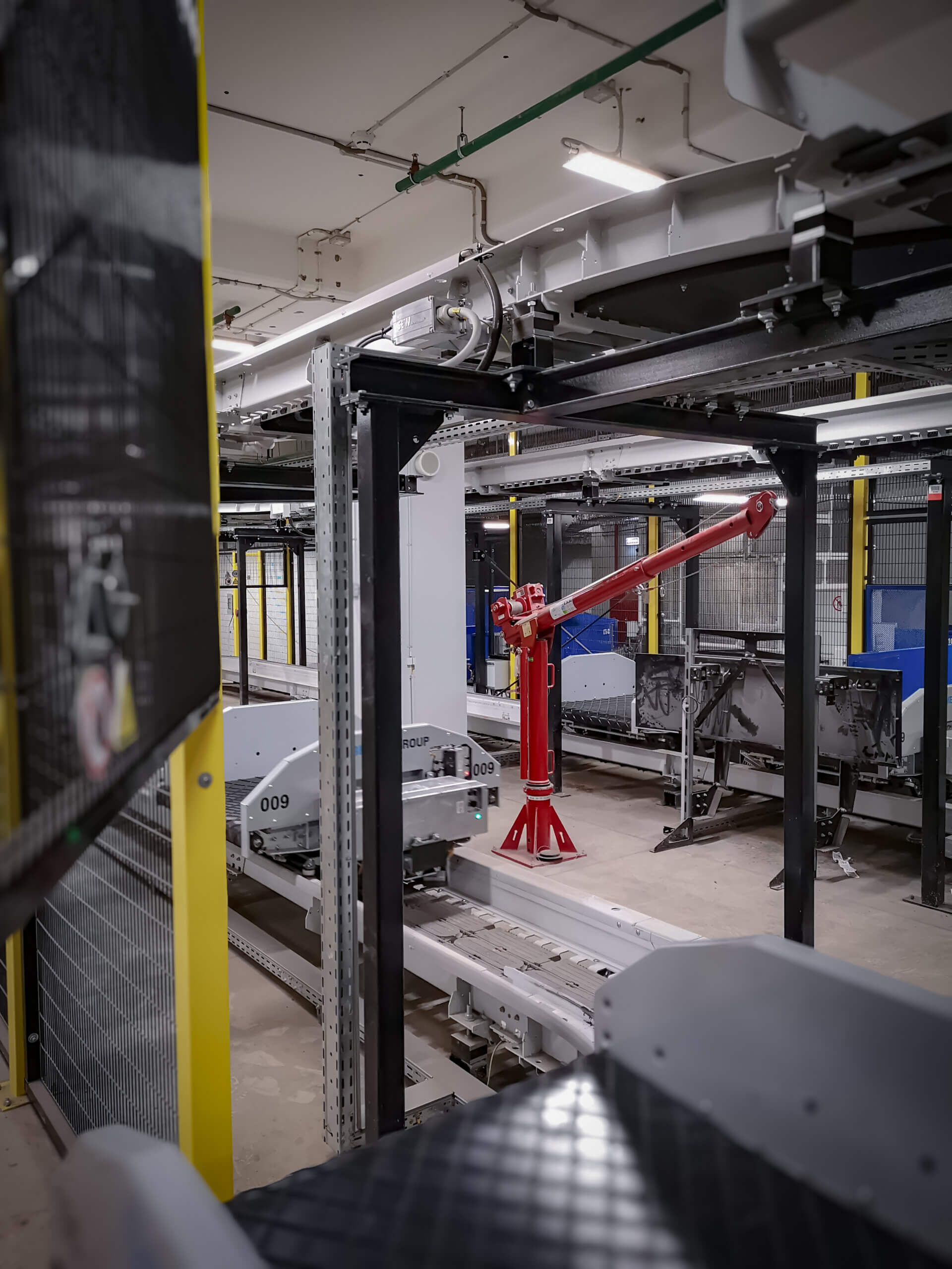 Red Thern portable davit crane mounted beside a white conveyor line in an industrial sorting facility