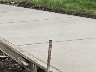 Fixed metal paving forms staked along freshly placed concrete flatwork