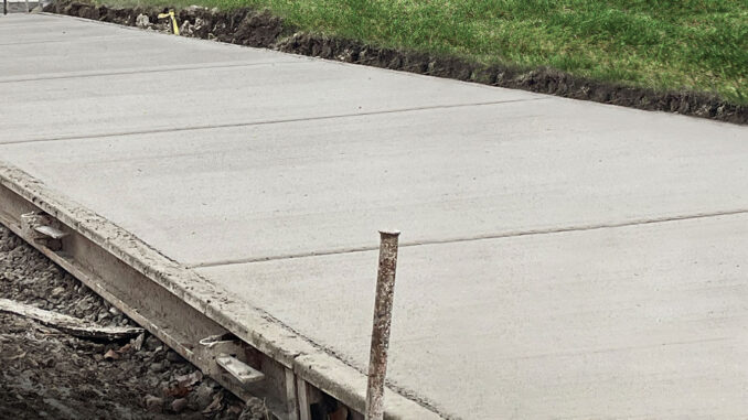 Fixed metal paving forms staked along freshly placed concrete flatwork