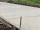 Fixed metal paving forms staked along freshly placed concrete flatwork