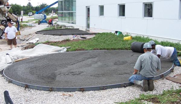 Workers finishing circular concrete pads formed with flexible metal radius forms