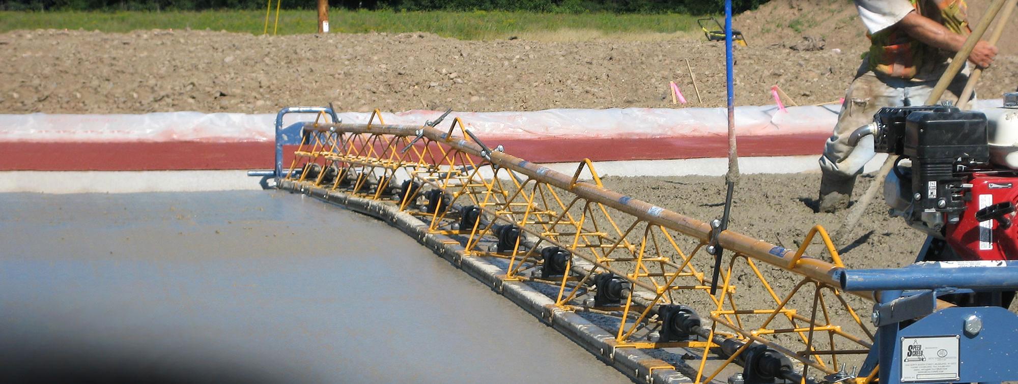 Yellow vibrating truss screed finishing concrete between fixed metal forms