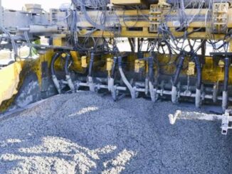 Yellow slipform paver underside with a row of paving vibrators in wet highway concrete