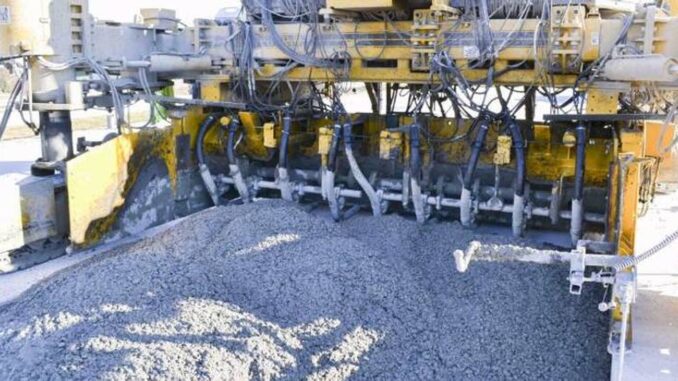 Yellow slipform paver underside with a row of paving vibrators in wet highway concrete